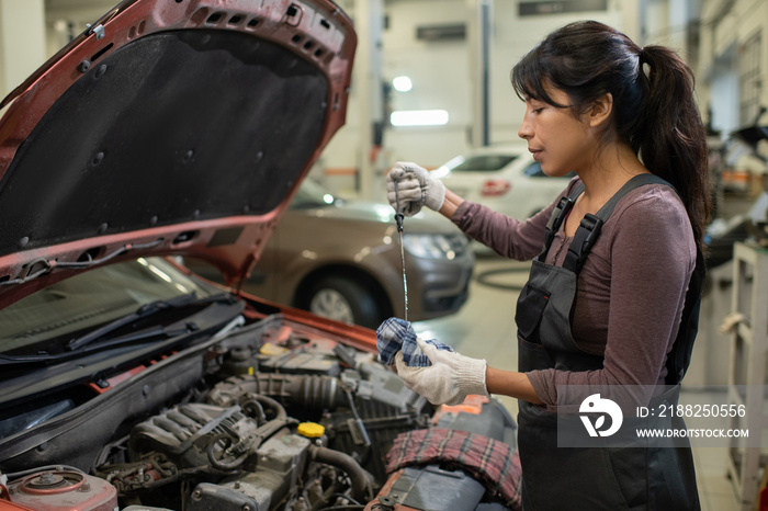 Side view portrait of young female mechanic checking oil levels while repairing car in workshop, copy space