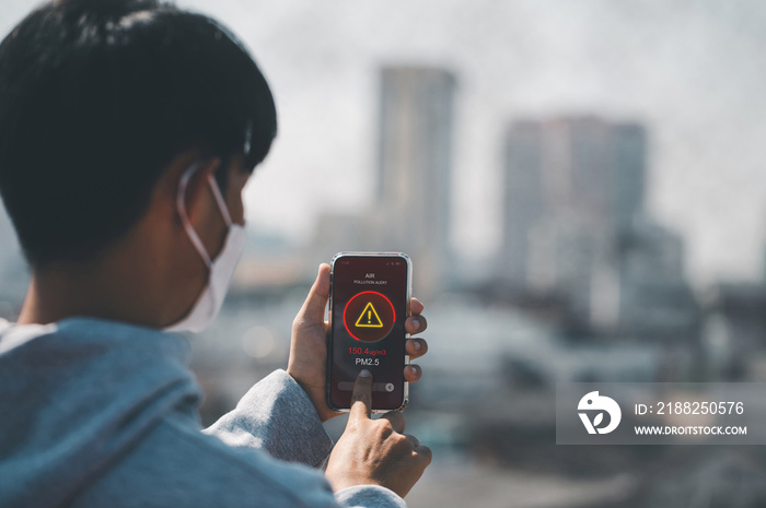 Man wearing the N95 Respiratory Protection Mask and using a smartphone app showing PM 2.5 dust in the capital that exceeds the standard that is harmful to health. air pollution concept, pm 2.5 warning