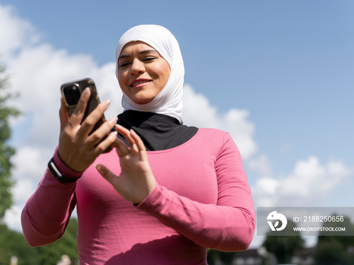 UK,Sutton,Woman in headscarf holding smart phone in park