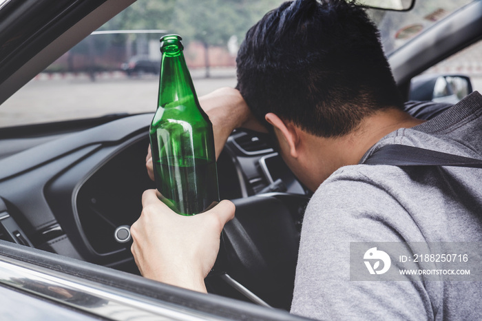 Young asian man drives a car with drunk a bottle of beer and fall asleep behind the wheel of a car