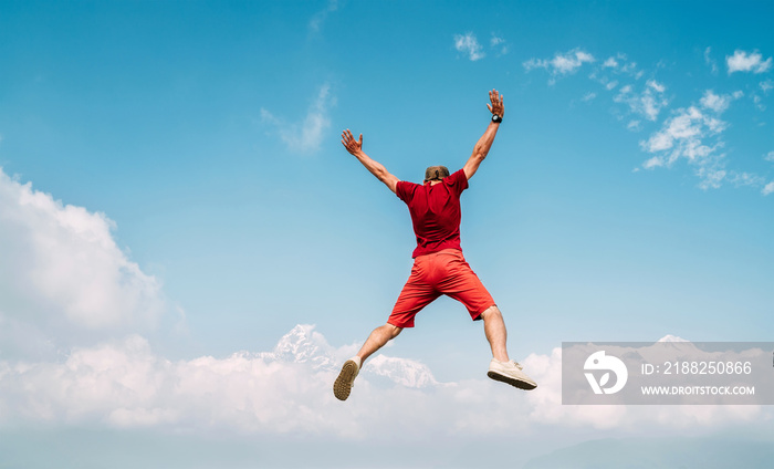 Happy man dressed red jumping over the clouds with Annapurna range mountains on background as he had trekking to Shanti (Peace) Stupa in Pokhara, Nepal.