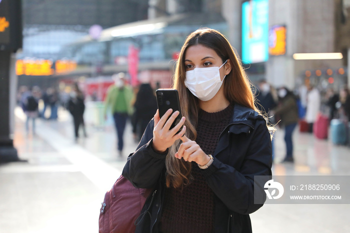 Student girl wearing protective mask buying ticket online with smartphone app at train station