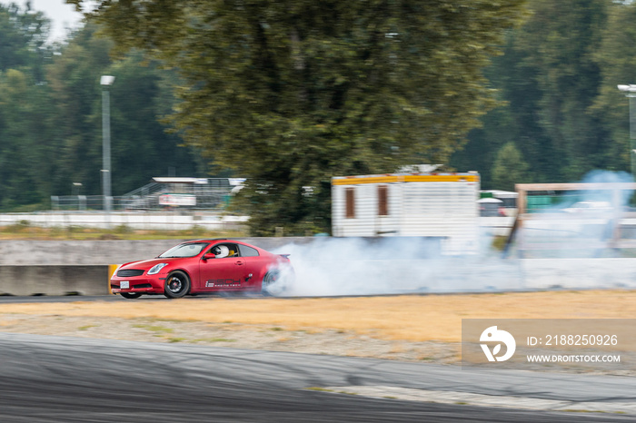 Red Drift Car / Race car drifting around corner very fast with lots of smoke from burning tires on speedway / racetrack / drift track. Infiniti g35 v8. JDM car. Luxury red sport car.