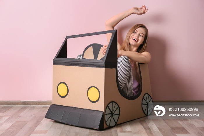 Young woman playing with cardboard auto near color wall. Concept of buying new car