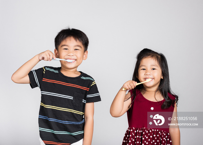 Little cute kid boy and girl 3-6 years old brushing teeth and smile in studio shot isolated on white background, happy Asian children holding toothbrush in mouth by himself, Dental hygiene healthy