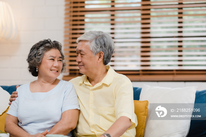 Asian elderly couple holding their hands while taking together in living room, couple feeling happy share and support each other lying on sofa at home. Lifestyle Senior family at home concept.