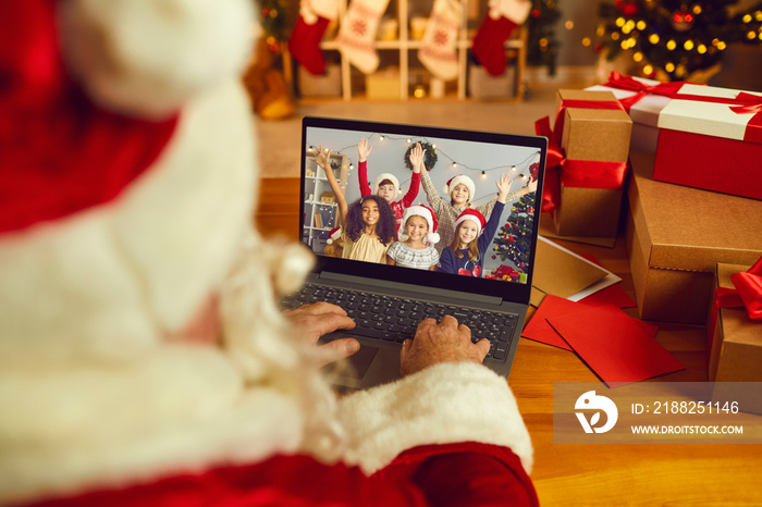 Santa Claus having video call with happy kids on laptop computer in his workshop