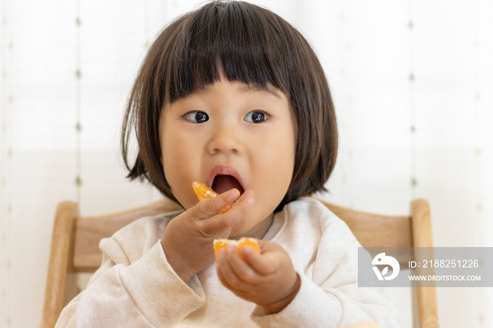 座ってミカンを食べる赤ちゃん（2歳4か月、女の子、日本人）