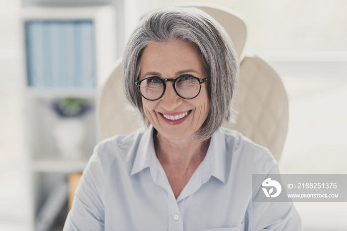 Photo portrait of mature senior woman employee experience expert toothy beaming smile businesswoman sitting at bright modern work station