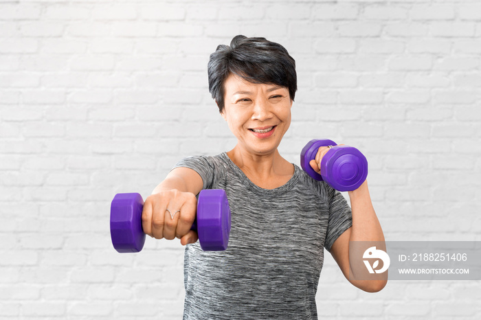 Attractive senior fitness Asian woman exercise and training. Elder exercising at home gym or fitness with dumbbells over white bricks wall background. Active older exercise and workout concept