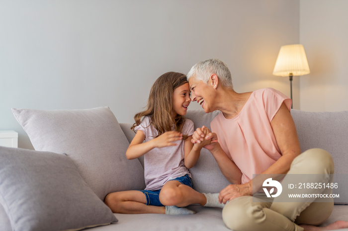 Happy middle-aged mature grandma and little preschool granddaughter touching noses laughing together, smiling loving old grandmother granny and cute carefree grandkid girl having fun playing at home