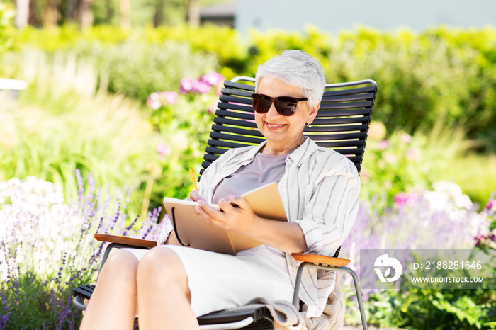 old age, retirement and people concept - happy senior woman with diary sitting in chair at summer garden