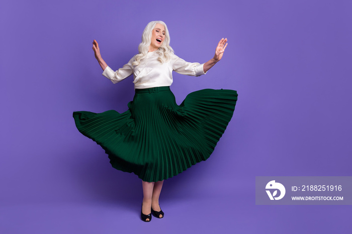 Full body photo of attractive mature grey haired lady dancing retro party raise hands modern movement excited wear white blouse green long skirt flying isolated purple color background