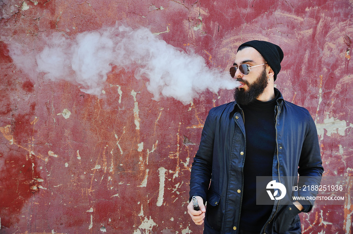 Young stylish bearded man in a black hat with an electronic cigarette or vape