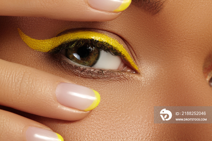 Close-up Female Eye with bright yellow Eyeliner Makeup. Neon Disco make-up and Fashion Manicure. Summer beauty style