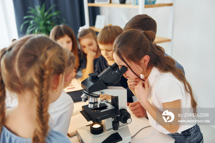 Girl looking into microscope. Group of children students in class at school with teacher