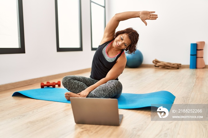 Middle age hispanic sporty woman having online fitness class at sport center.