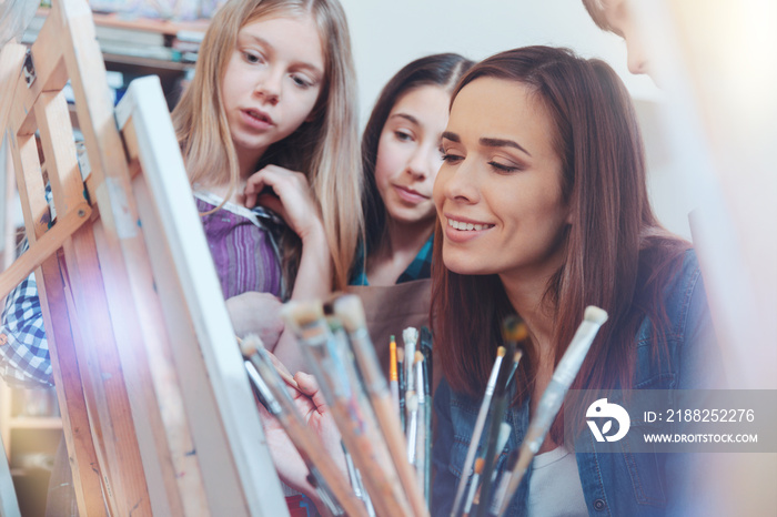 You should paint like this. Focused youngsters staring at their teacher of art sitting at an easel and working on a new masterpiece with oil pants.