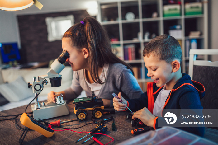 Happy smiling boy and girl constructs technical toy and make robot. Technical toy on table full of details