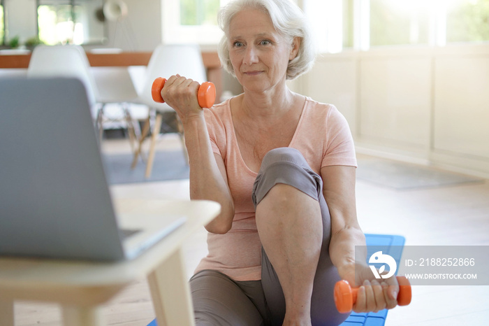 Senior woman doing fitness exercises at home through virtual class