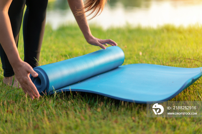 Young asian woman rolling blue yoga mat or fitness mat prepare to exercise in park, Healthy concept, Mind-body improvements concept.