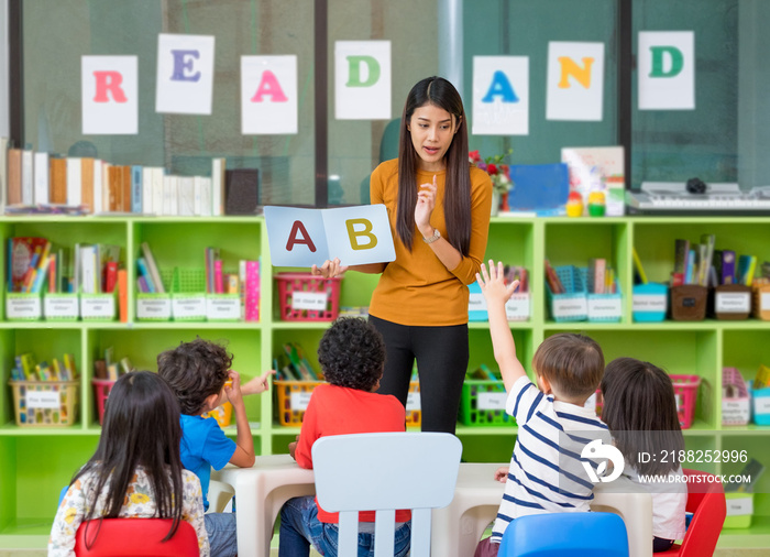 Asian female teacher teaching and asking mixed race kids hand up to answer in classroom,Kindergarten pre school concept.