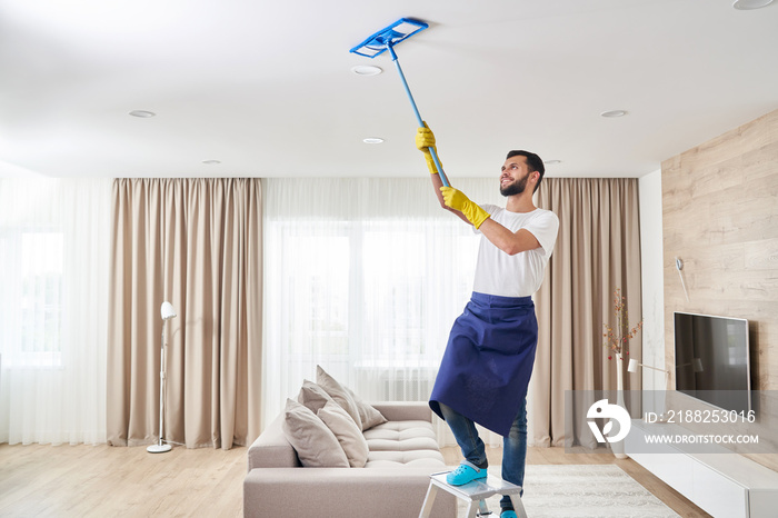 Man cleaning ceiling and lamps in living room. House cleaning service concept.