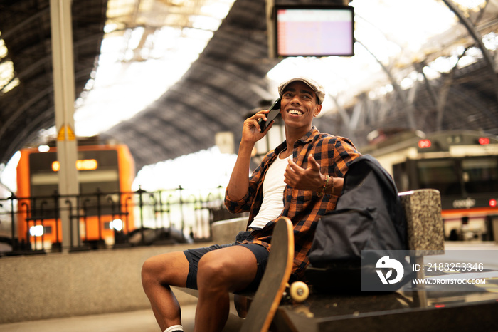 Happy young man waiting for the train. African man waiting in a subway. Man using a phone.