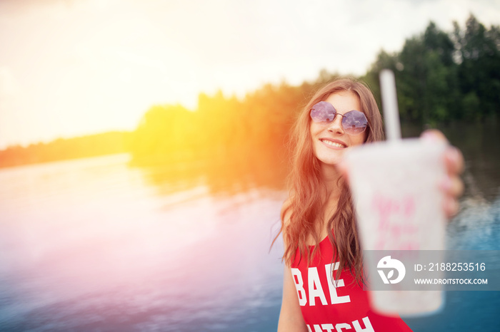 Young woman in red swimsuit holds glass with cocktail on beach