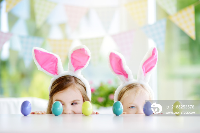 Two cute little sisters wearing bunny ears playing egg hunt on Easter