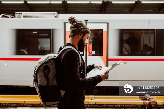 .Attractive young man with beard waiting at the train station in Vienna. Thinking about his trip, with the map in his hand and a backpack. Travel photography.