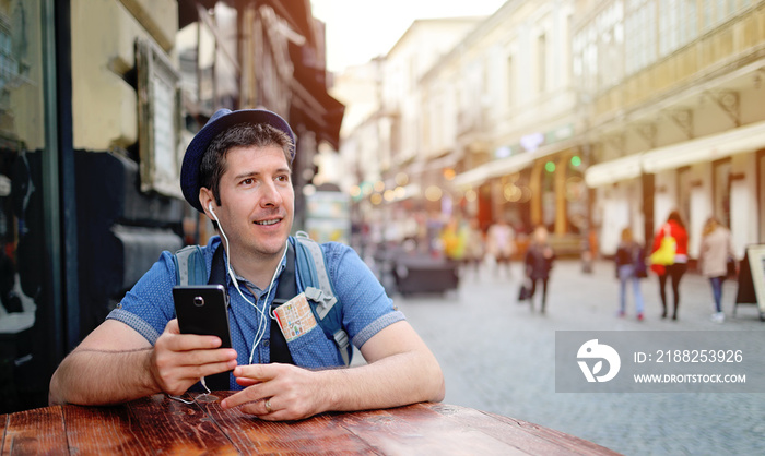 Young man travelling alone on streets of European city, using smartphone. Free roaming calls abroad. Unrecognisable People walking behind on the street