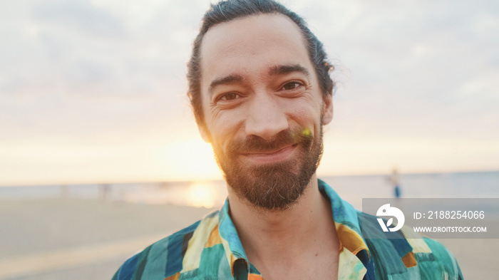 Close-up of young smiling man looking at the camera on the beach at sunrise