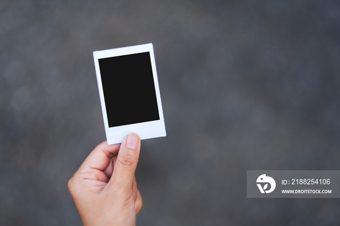 A hand holding mockup of polaroid photo frame with blurred background