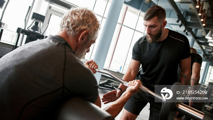 Senior powerlifter training with professional assistance in gym