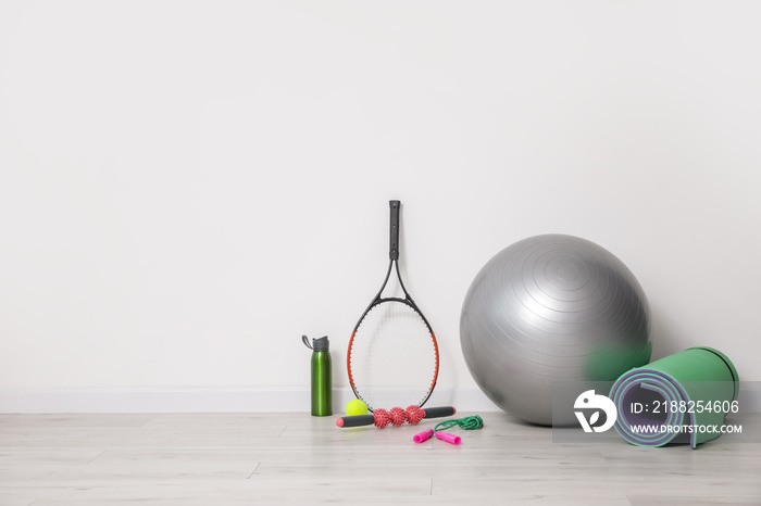 Set of sports equipment with fitness ball near light wall