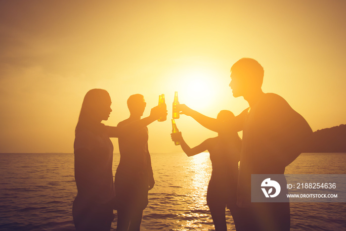 Silhouette of people having party, claging beer bottles at the beach in sunset