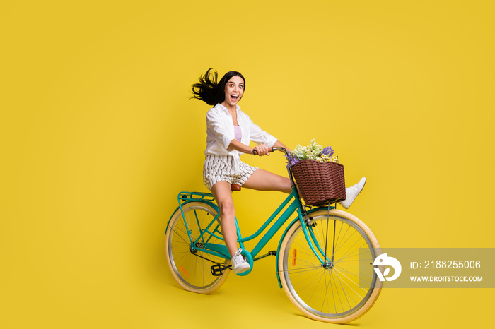 Full size photo of young happy cheerful excited girl extremely riding bicycle isolated on yellow color background