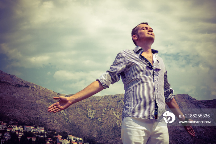 Enjoying in freedom and fresh air. Carefree man with arms outstretched against mountains and sky.