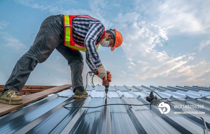 Construction expertise worker wear safety uniform install new roof,Roofing tools,Electric drill used on new roofs with Metal Sheet.worker roofer builder working on roof structure.