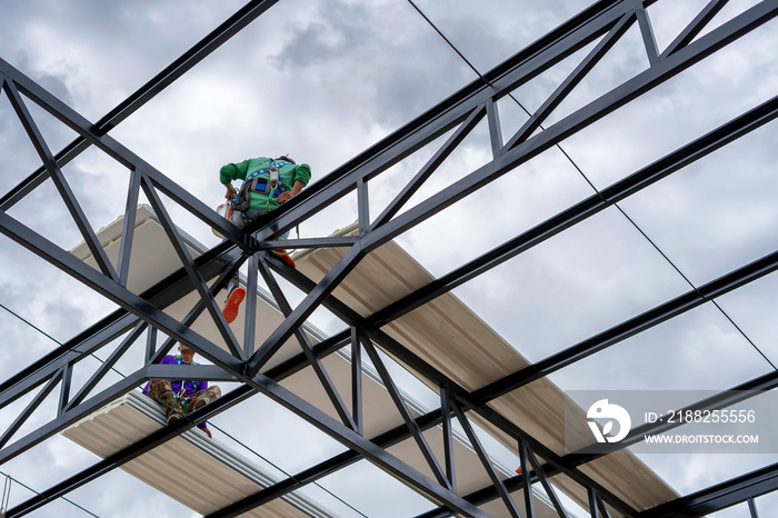 Construction workers wearing yellow plastic helmets and seat belts are installing the factory roof with white PU metal sheet.