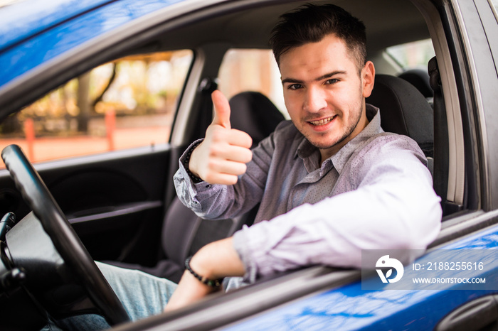 Happy smiling man sitting inside car showing thumbs up. Handsome guy excited about his new vehicle. Positive face expression