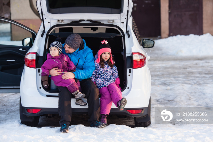 father with kids sit on the car trunk