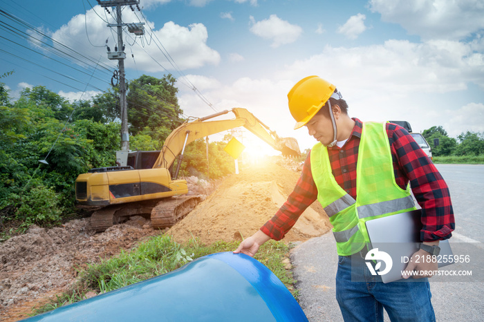 Engineer wear safety uniform hold a laptop examining excavation the large pipe patch and Plumbing water system underground at construction site.