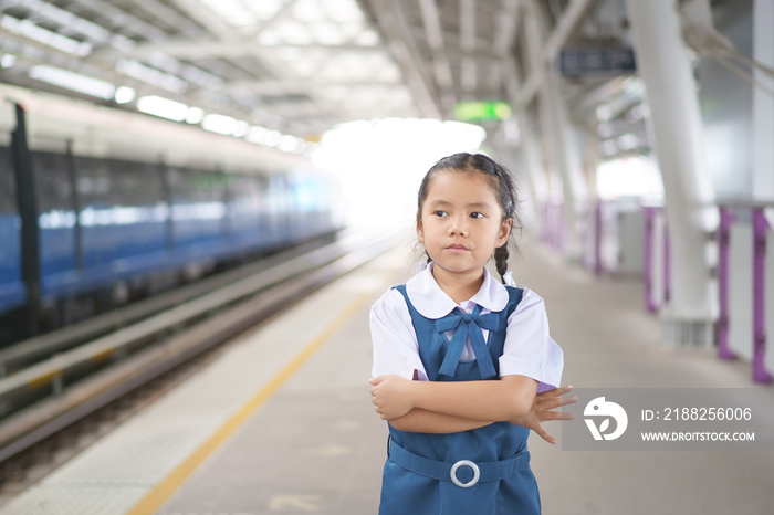 Asian child student traveling or kid girl waiting sky train or electric train and railways or metro subway on railway station or platform in street city for back to school transport with arms folded