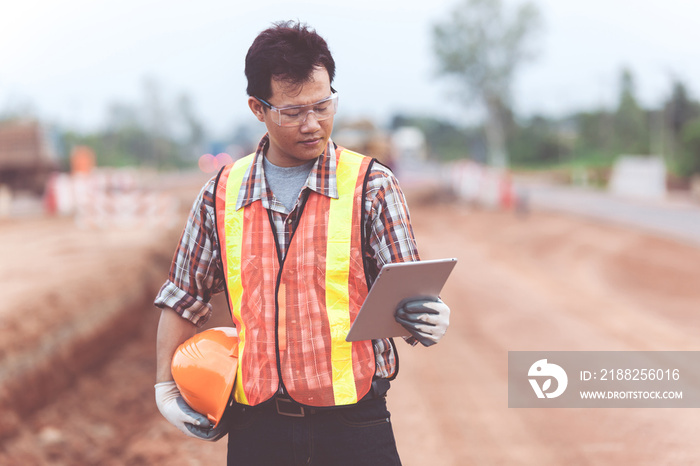 Asian engineer with hardhat using tablet inspecting and working at construction site