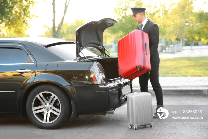 Chauffeur putting suitcase in car trunk