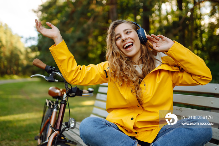 Pretty young womanusing mobile phone in the city while listening music through earphones to go by the bicycle in the park. Lifestyle. Relax, nature concept.