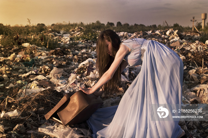 Girl among landfill pulling heavy suitcase