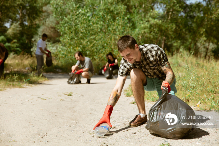 Sweet hearts rescue the planet. Group of volunteers tidying up rubbish on beach in sunny day. Young men and women take care of nature and environment, taking bottles and packs away. Concept of ecology